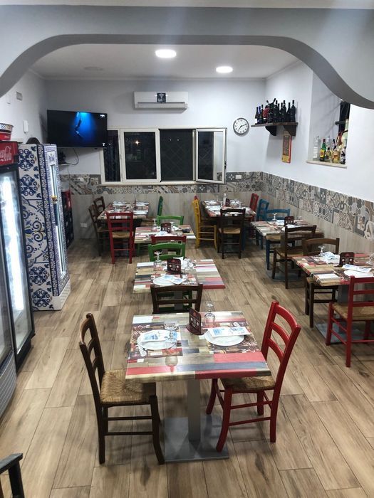 Interno del ristorante con tavoli e sedie, pavimenti in legno e sedie colorate.