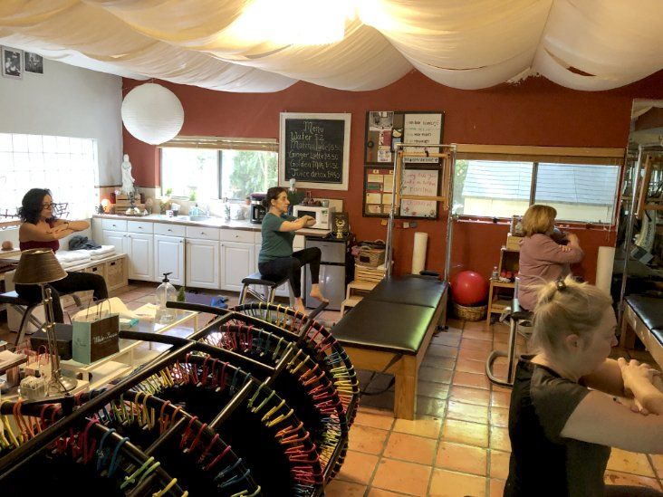 A woman is sitting on a Pilates table in a room with other people