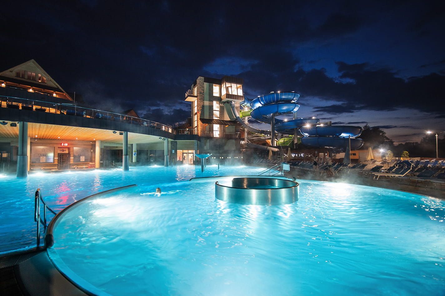 Outdoor thermal pool with a round whirlpool, lit up in the evening at Chocholow Thermal Baths