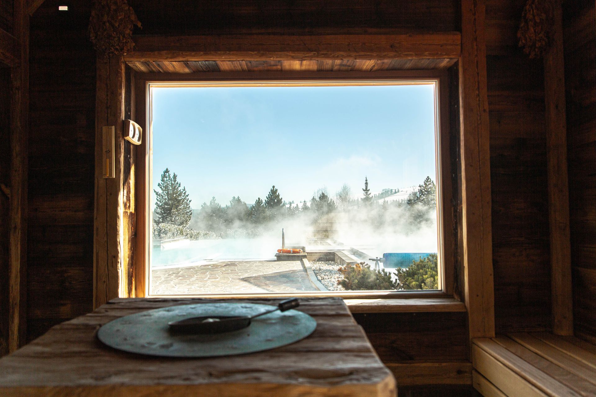 View from a wooden sauna window onto steaming outdoor pools at Terma Bania
