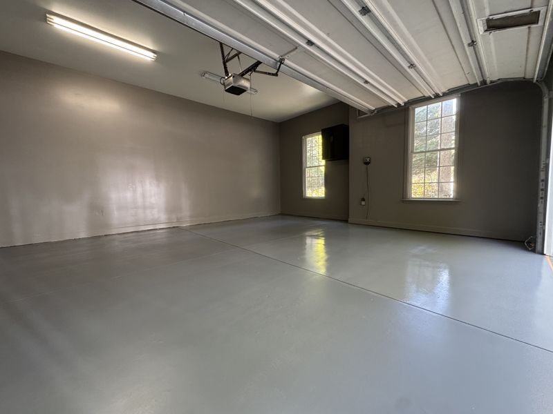 Empty garage with gray floor, beige walls, and two windows letting in daylight