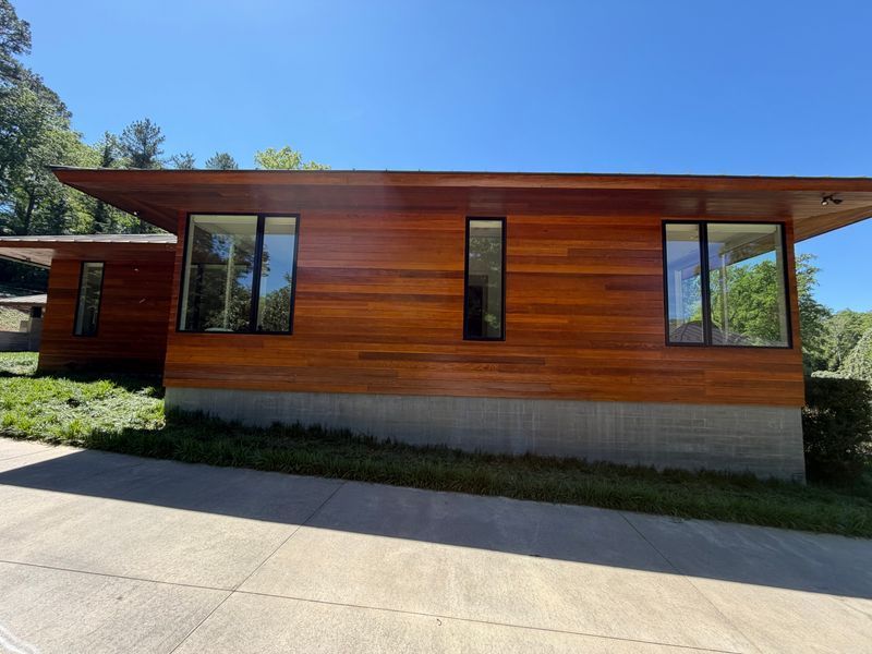 Modern wood-sided house with large windows and a concrete foundation on a sunny day