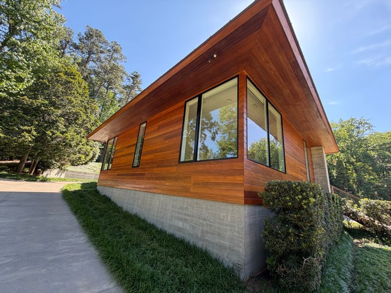Modern wooden house with large windows and a sloped roof on a grassy hillside.