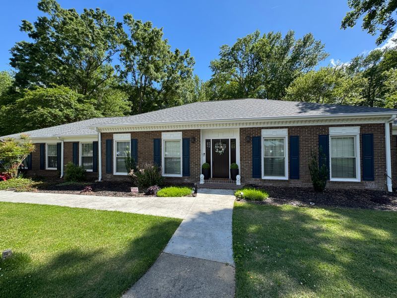 Single-story brick house with white trim, front walkway, and green lawn under a blue sky