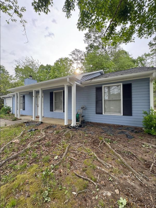 Blue house with white porch columns and overgrown yard after storm damage
