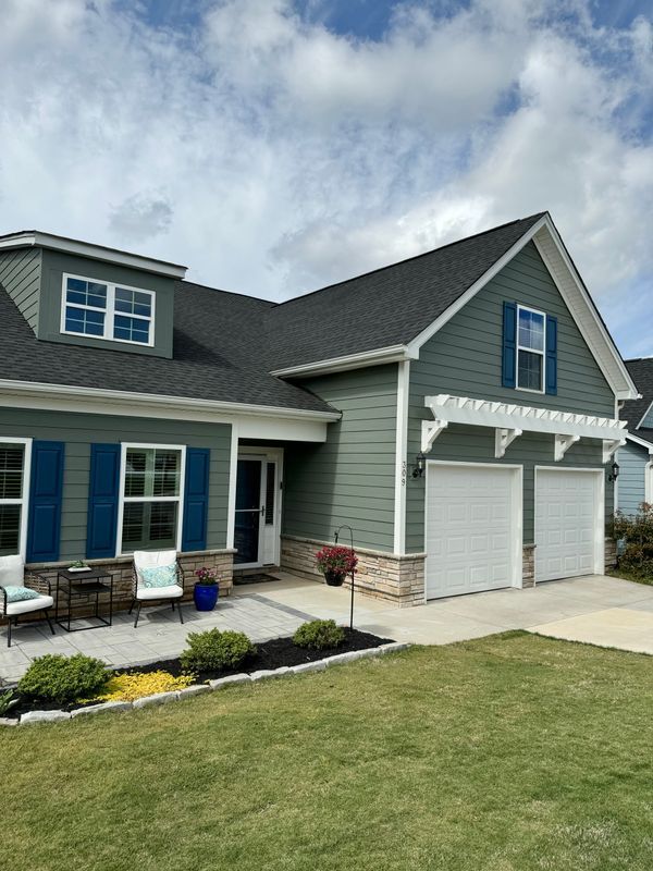 Suburban house exterior with blue shutters, white garage doors, and a front lawn under a partly cloudy sky