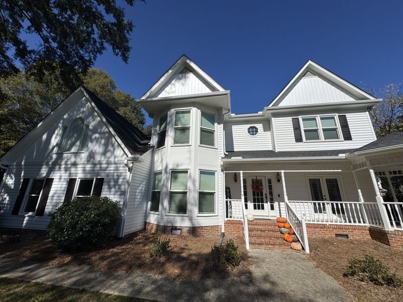 White Victorian-style house with wraparound porch, bay window, and brick steps under a blue sky