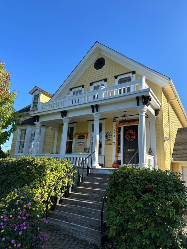 Yellow house with white porch columns, black shutters, and front steps under a blue sky