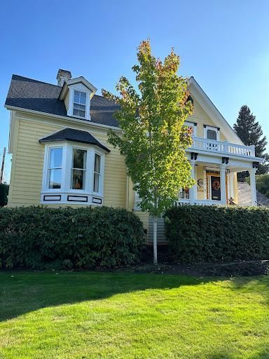 Yellow house with white trim, a porch, and a large tree in front under a clear blue sky