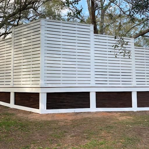 White slatted fence-like enclosure on a wooden structure in a grassy yard under trees