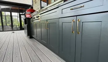 Modern outdoor kitchen with dark cabinets, brass handles, and a built-in grill on a deck