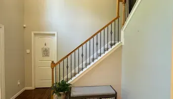 Staircase with wooden banister in a beige hallway, with a bench and potted plant near a framed wall print