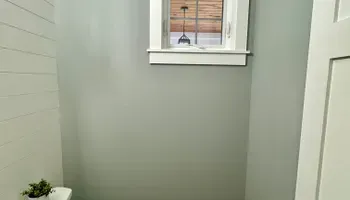 Narrow gray hallway with a small window and white trim, plus a closed door on the right.