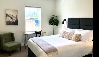 Bright bedroom with a king bed, green chair, small desk, wall art, and a window with city view.