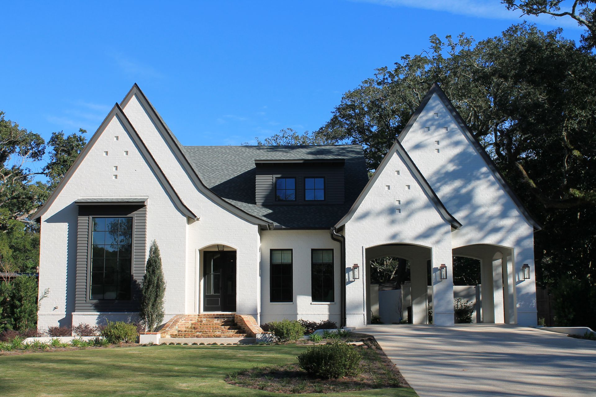 Modern white house with dark roof, arched entry, and a driveway under a blue sky