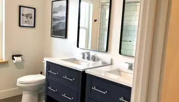 Bathroom vanity with dark cabinets, white countertop, sink, mirror, toilet, and framed wall art.