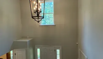 Stairwell with a large black chandelier, white walls, and a small window above a front door.