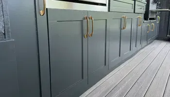 Gray kitchen cabinets with brass handles along a wood plank floor in a modern interior