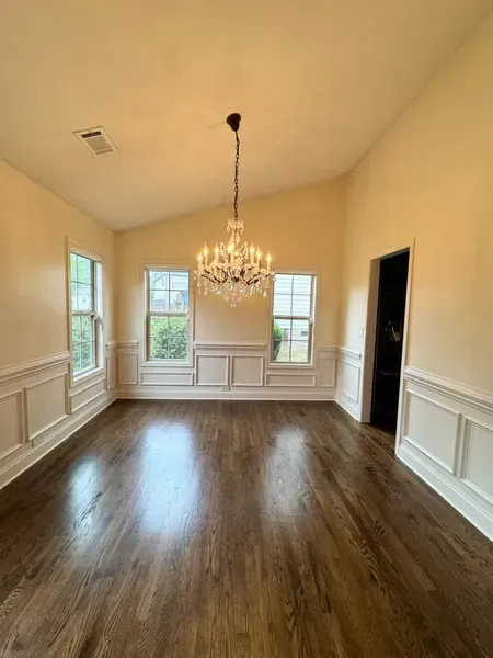 Empty dining room with chandelier, dark wood floors, white trim, and three windows.