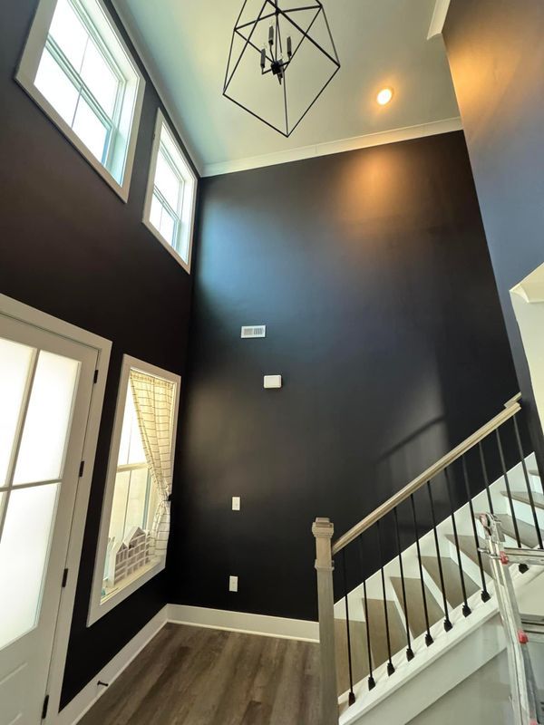 Tall foyer with dark walls, wood floor, staircase, and large windows letting in natural light
