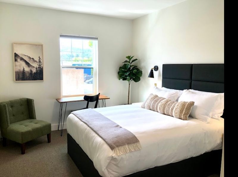Bright bedroom with a bed, green chair, desk by the window, and a potted plant