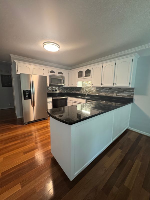 Bright white kitchen with stainless steel appliances, dark countertops, and glossy hardwood floors