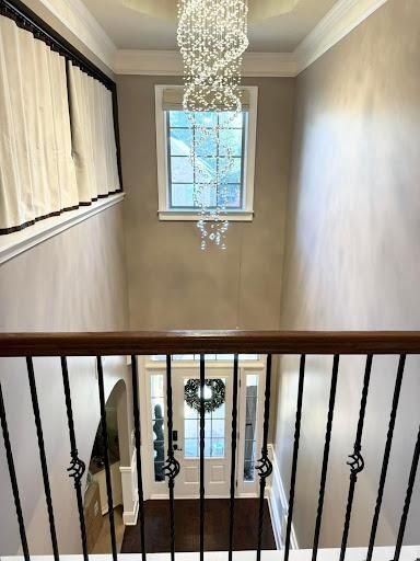 Stairwell with black railing, beige walls, chandelier, and a window at the landing