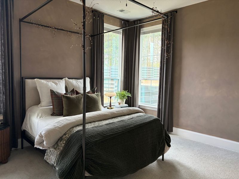 Modern bedroom with a canopy bed, dark bedding, and floor-to-ceiling windows with sheer curtains.
