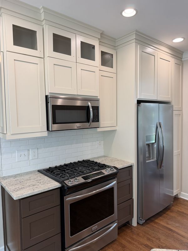 Modern white kitchen with stainless steel stove, microwave, and French-door refrigerator, plus dark lower cabinets.