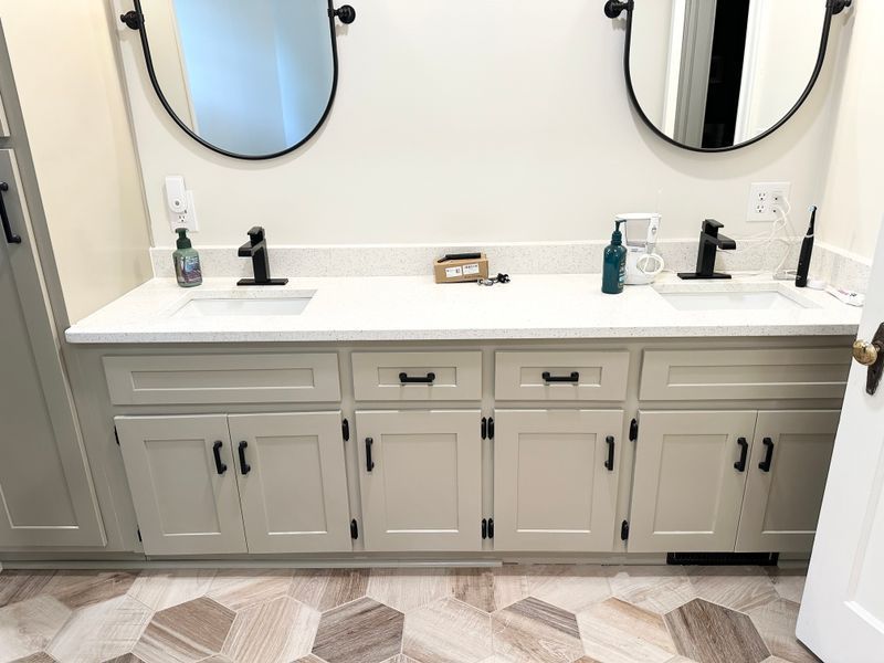 Bathroom vanity with double sinks, mirrors, black faucets, and gray cabinets under a white countertop