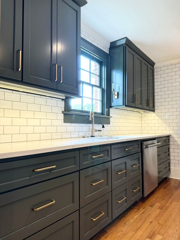 Modern kitchen with dark cabinets, white subway tile backsplash, window over sink, and wood floors