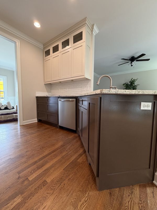 Modern kitchen with dark cabinets, white upper cabinets, wood floors, and a large island with sink and pendant lighting