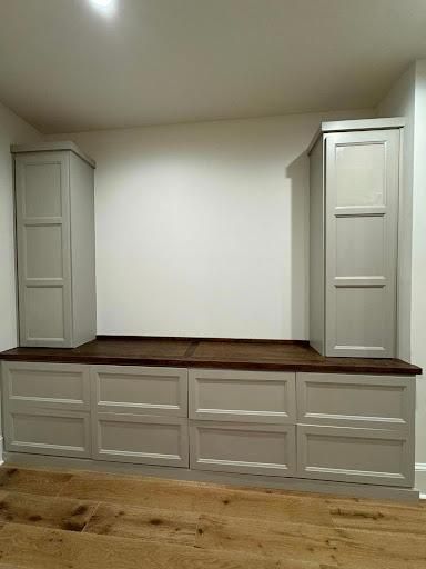 Built-in white cabinetry with wood countertop and tall side cabinets in a room with hardwood floor.