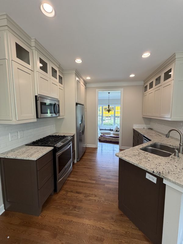Bright white galley kitchen with dark cabinets, stainless appliances, and wood floors leading to a patio door.