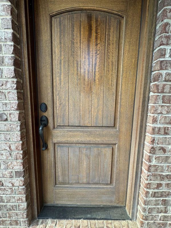 Wooden front door with black handle, set in a brick entryway