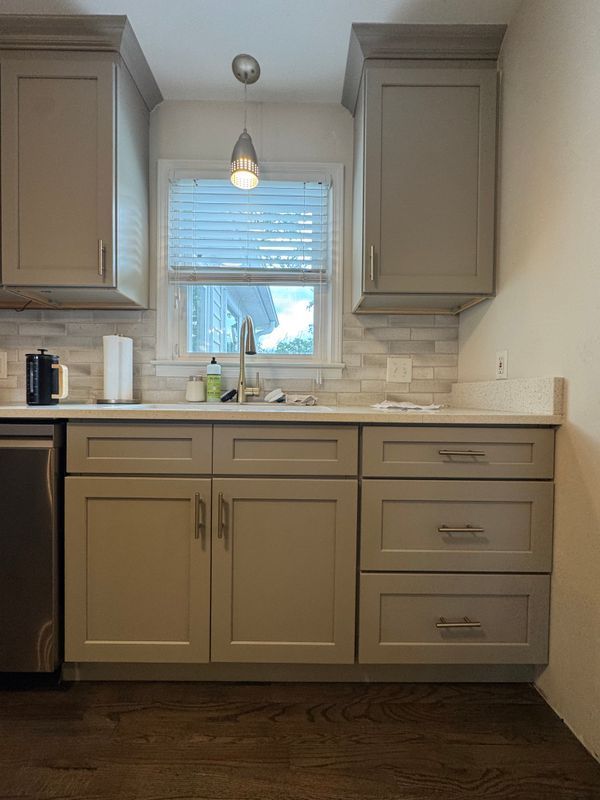 Small kitchen with beige cabinets, white countertops, window over sink, and pendant light.