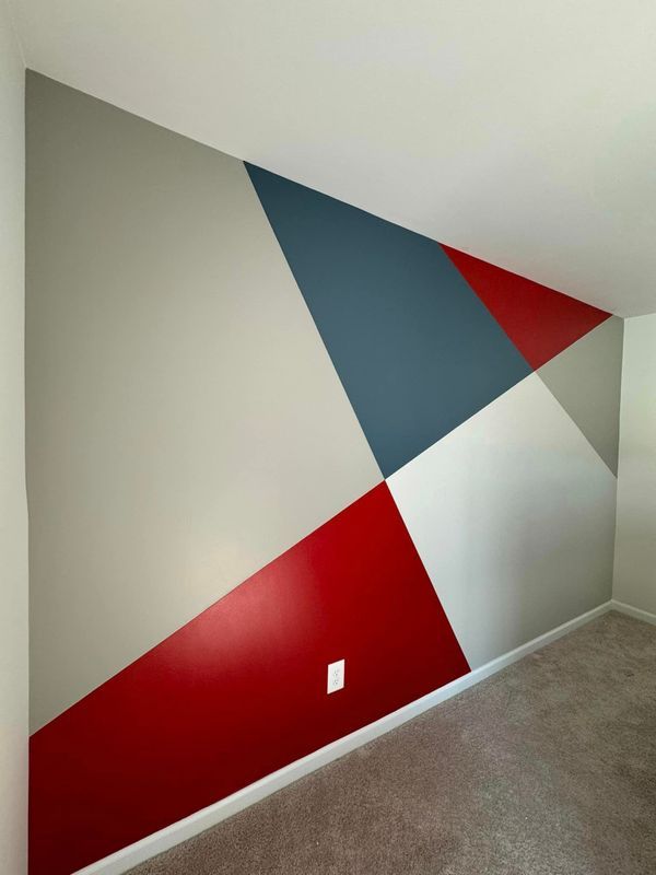 Geometric mural with red, blue, gray, and white triangles on an interior wall above carpet.