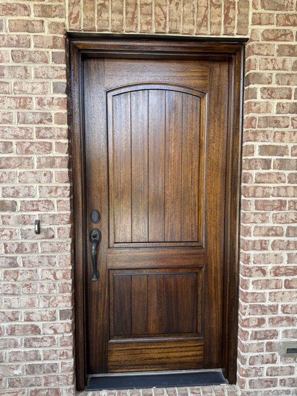 Wooden front door with arched panels set in a brick exterior wall