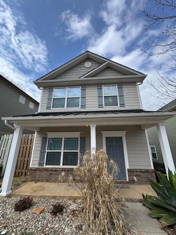 Two-story gray house with white trim, front porch, and cloudy sky above
