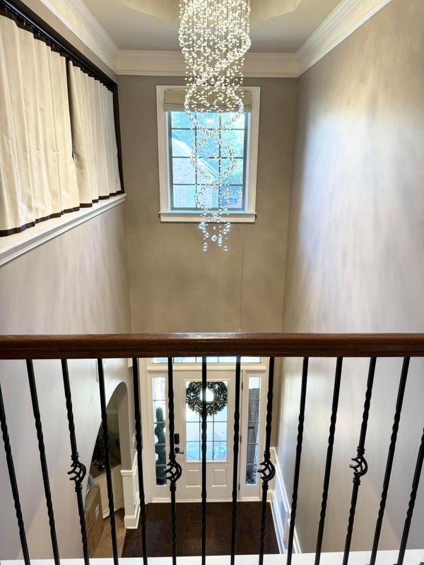 Stairwell with black railing, hanging crystal chandelier, and a window at the landing.