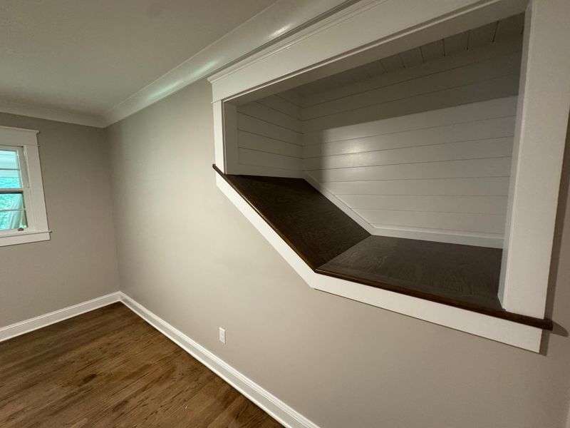 Bedroom with a built-in desk nook, dark wood surface, beige walls, and wood flooring.