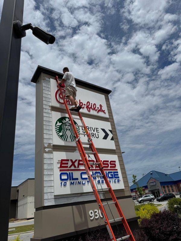 Worker on a red ladder painting a Starbucks sign on a roadside billboard.