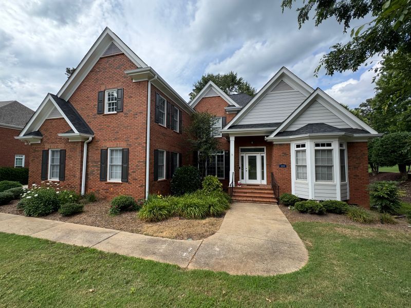 Brick and white suburban house with front porch, curved walkway, and landscaped yard