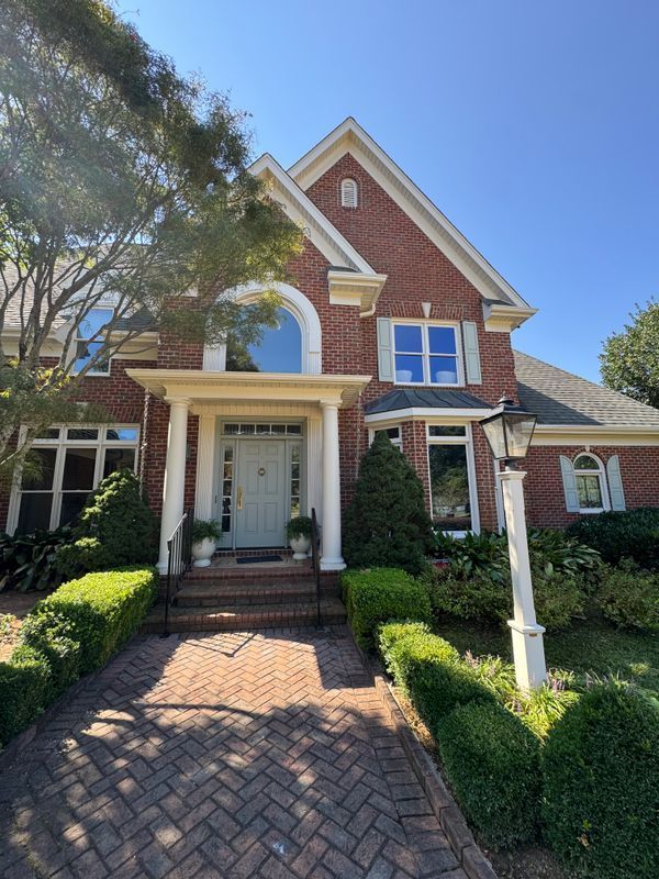 Brick house with white trim, front porch, and landscaped walkway under a blue sky