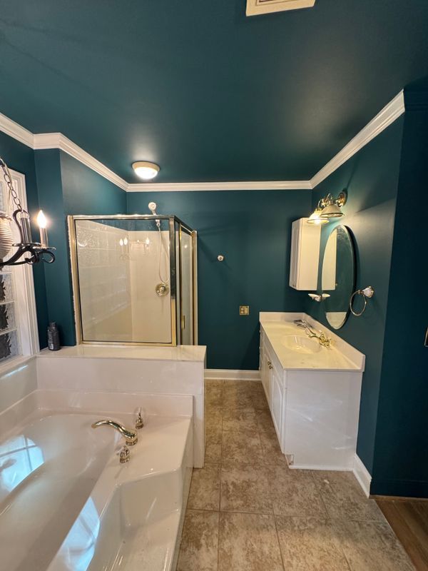 Teal bathroom with a bathtub, glass shower, vanity, and mirror under wall sconces.