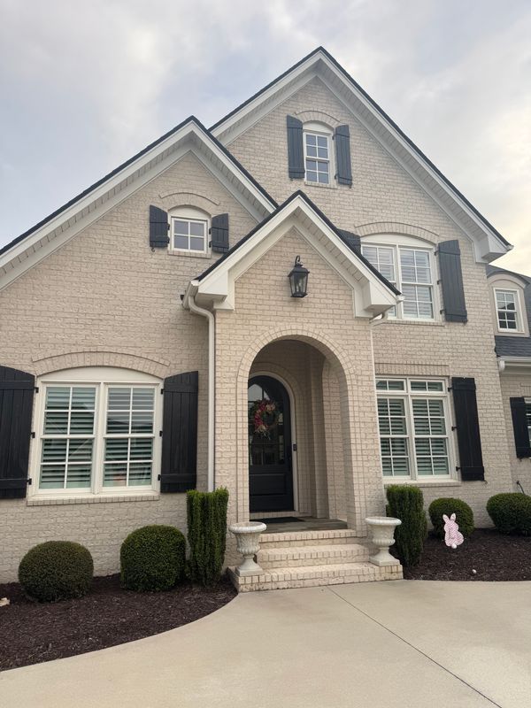 Two-story brick suburban house with arched front entry, black shutters, and manicured landscaping