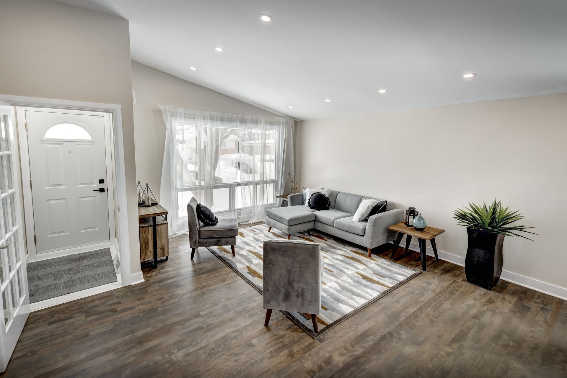 Bright modern living room with gray sofa, patterned rug, armchair, and large window by front door