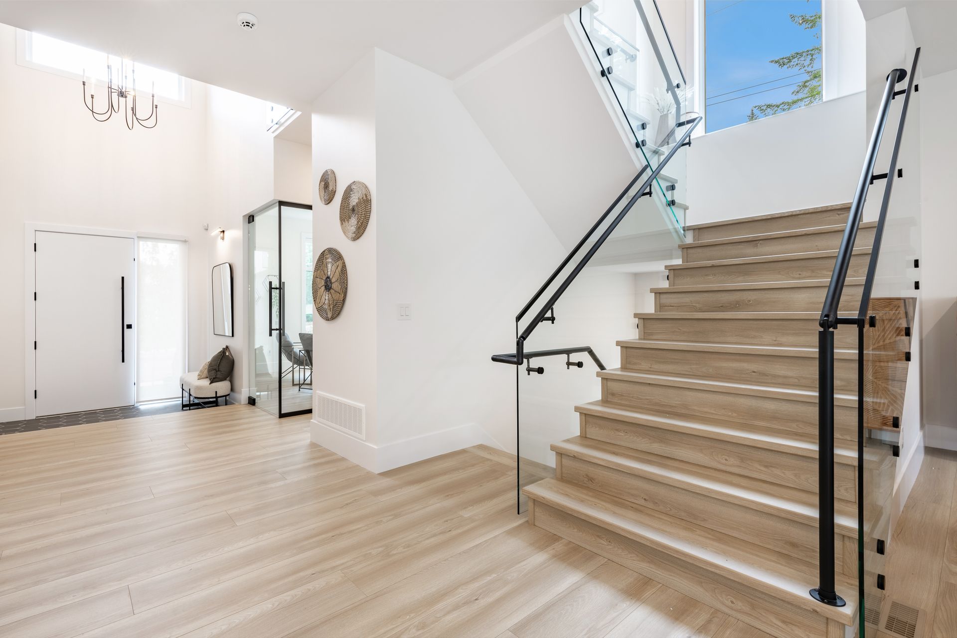 Bright foyer with light wood floors, white walls, a staircase, and a seating area with mirrors.