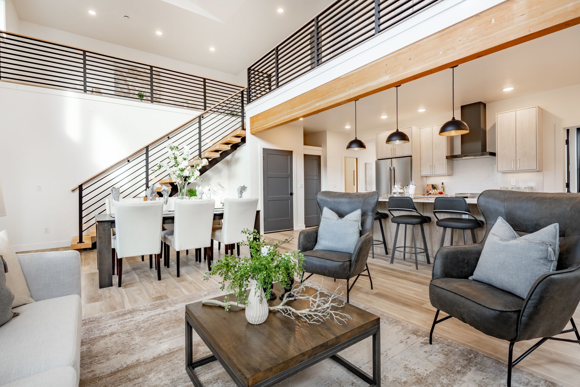 Bright open-concept living room and dining area with gray chairs, white table, staircase, and kitchen island