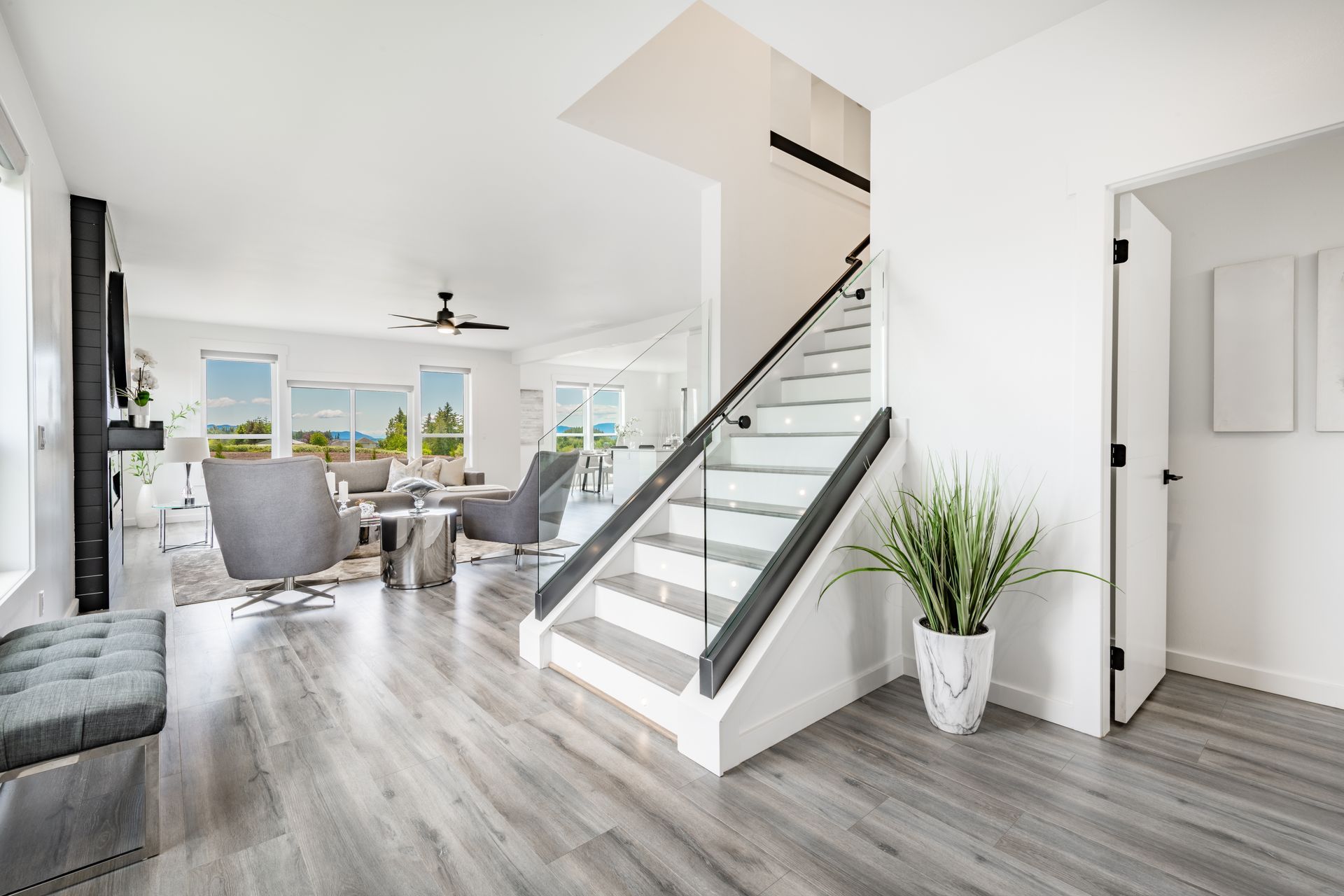 Bright open living room with stairs, gray floors, white walls, and city view through large windows